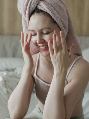 beauty, skin care, spa concept, young woman with a towel on head apply cream on face skin.