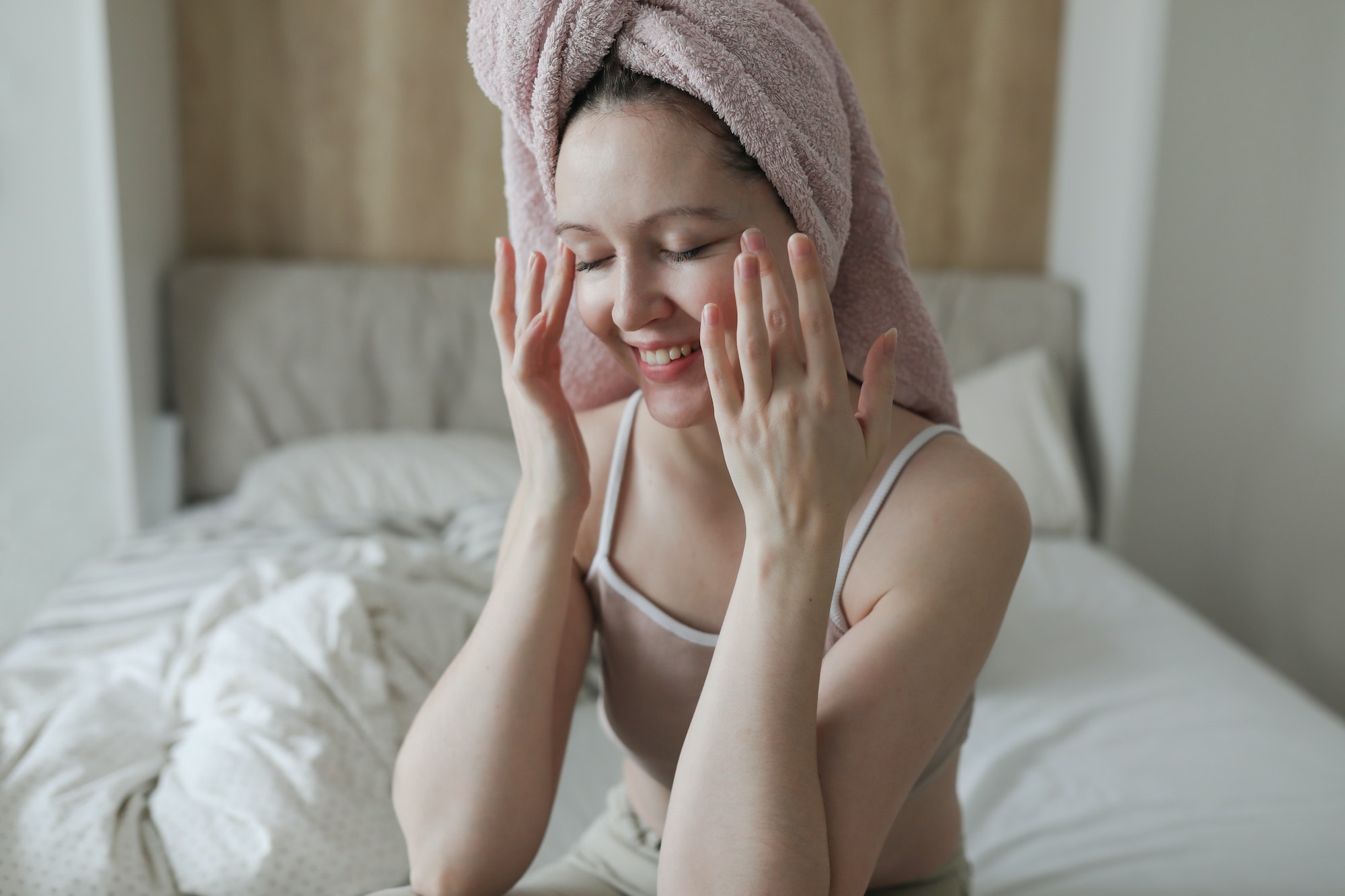 beauty, skin care, spa concept, young woman with a towel on head apply cream on face skin.